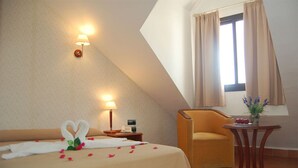 Una habitación de hotel con una cama, una silla, una mesita y una ventana con cortinas.