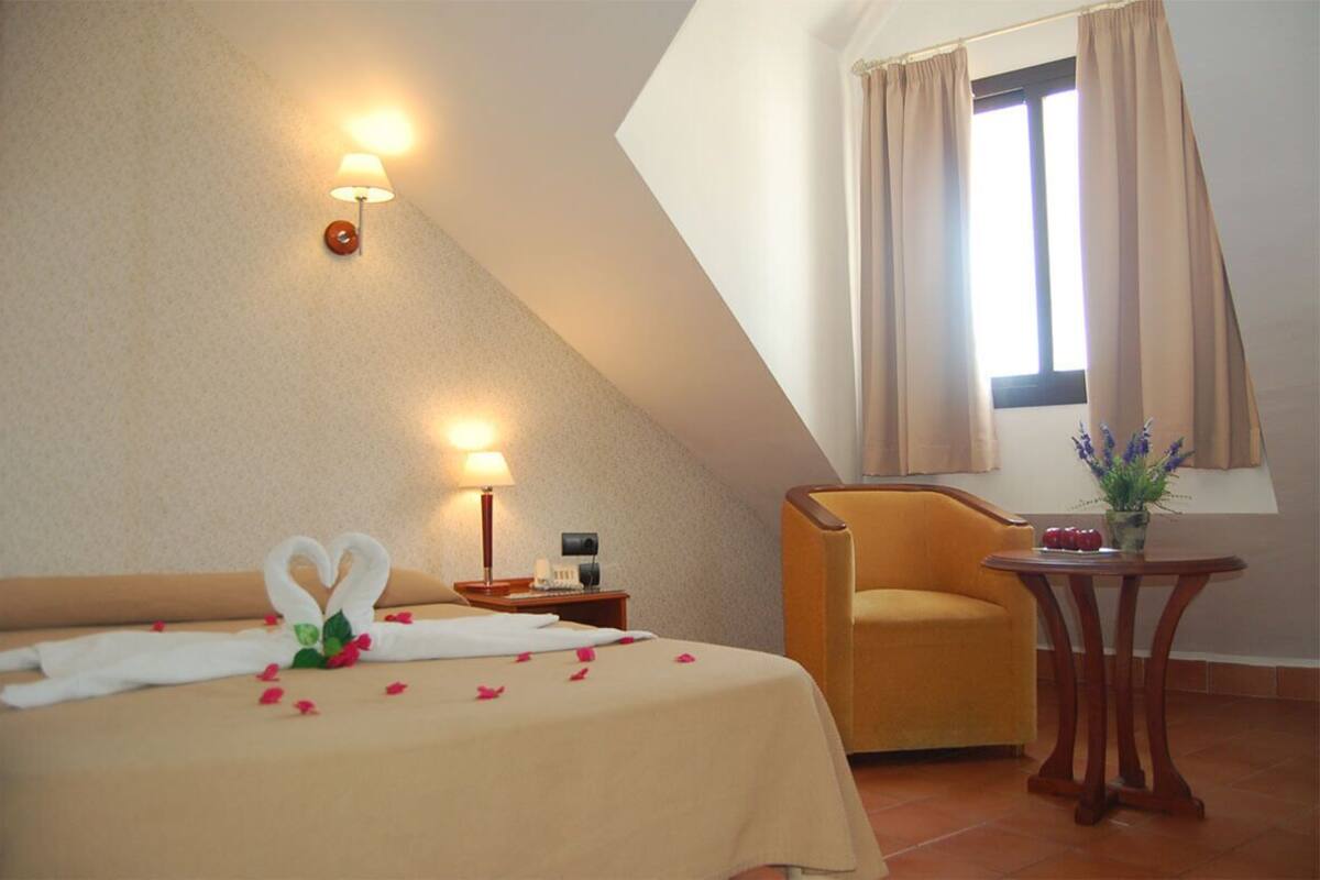 Una habitación de hotel con una cama, una silla, una mesita y una ventana con cortinas.