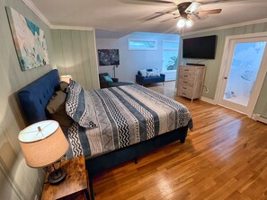 Una camera da letto con un letto, una ventola a soffitto, una TV, un comò e una porta che dà su un balcone.