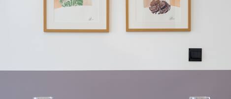 A dining table with two framed artworks, a light purple wall, and a wooden chair in the foreground.