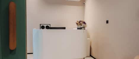 A reception desk with a white counter, a small plant, and a wall-mounted air conditioner.