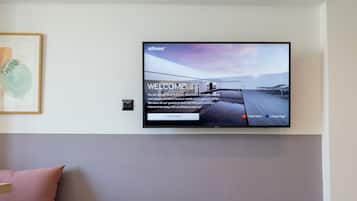Une chambre d’hôtel moderne équipée d’un téléviseur à écran plat fixé au mur, qui affiche un écran d’accueil, ainsi que d’un lit, d’une table de chevet et d’un climatiseur fixé au mur.