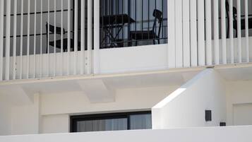 A modern building with a balcony featuring white railings and a window with a chair inside.