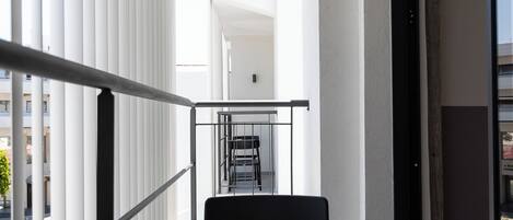 A balcony with a table and chairs, a railing, and a view of the street and buildings.