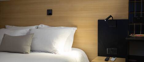 Ein Hotelzimmer mit einem hölzernen Kopfteil, einem Bett mit weißer Bettwäsche, einem Nachttisch mit Fernbedienung und einer Wandleuchte.