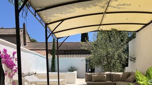 Un espace extérieur aménagé avec un coin salon abrité, comprenant un canapé blanc et une petite table, le tout entouré de verdure et d’un arbuste d’hortensia blanc.