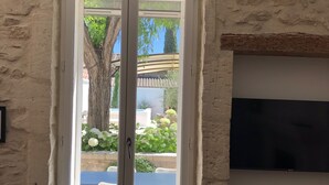 Un salon avec un mur en pierre, une grande fenêtre donnant sur un jardin et un téléviseur à écran plat fixé au mur.