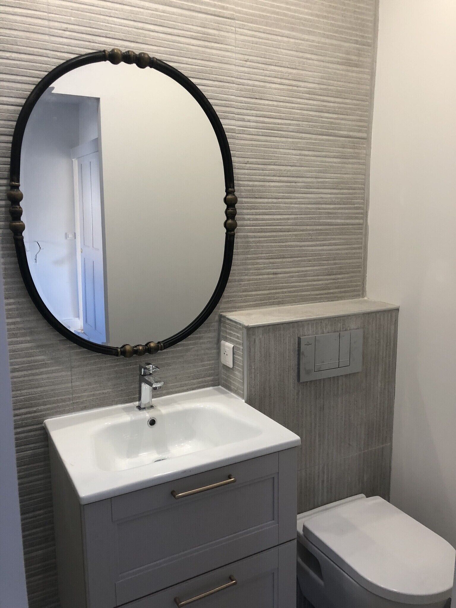 A bathroom with a white sink, a round mirror with a black frame, and a toilet.