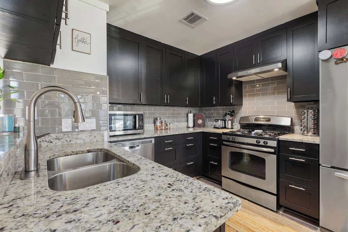 A modern kitchen with dark cabinets, stainless steel appliances, and a granite countertop.