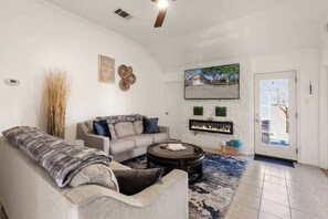 A living room with a sofa, coffee table, fireplace, and a door leading outside. - Luxury Modern 4BR | Hot Tub | Mins to DT & Rainey (Austin)