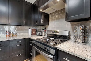 Una cocina moderna con armarios oscuros, estufa de acero inoxidable y salpicadero de azulejos.
