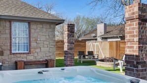 Una vasca idromassaggio in un giardino interno con muri in pietra, un patio in legno e una recinzione di legno.