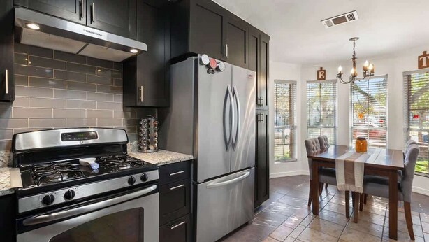 Una cucina moderna con mobili scuri, elettrodomestici in acciaio inossidabile e un'area pranzo con tavolo e sedie.