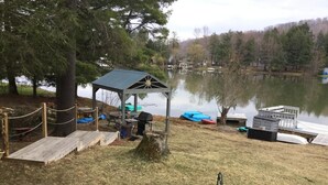 A lakeside gazebo with a small deck, surrounded by a rope fence, near a dock with boats.