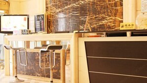 Un'area reception con un bancone in marmo, due sgabelli da bar, una televisione e un cartello con caratteri giapponesi.