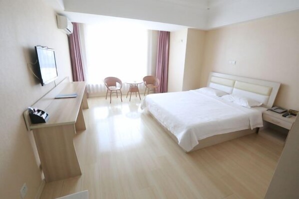 A hotel room with a bed, a desk, two chairs, a TV, and a window with curtains.