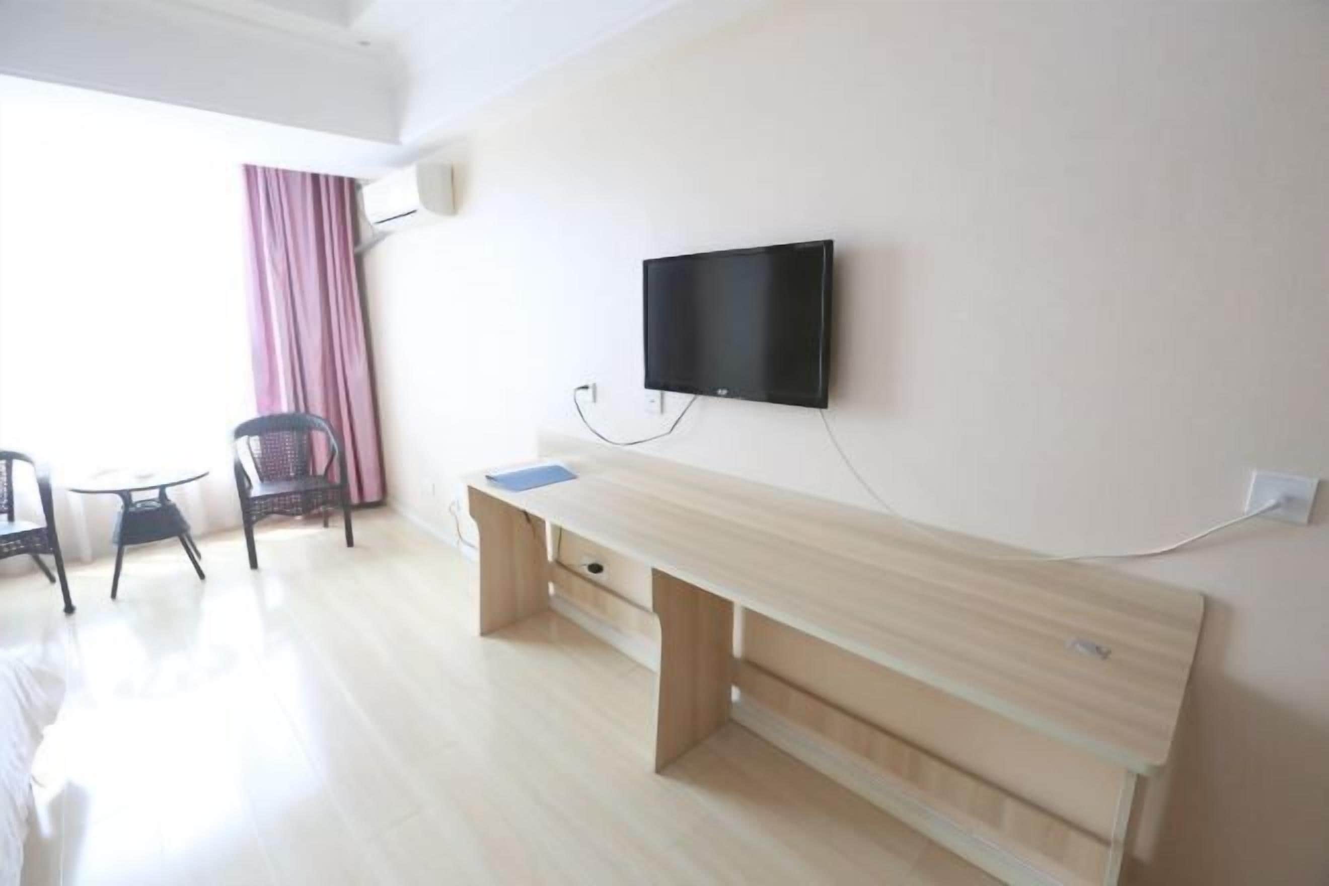 Una habitación con un escritorio de madera, un televisor montado en la pared, una silla y una ventana con cortinas.