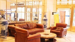 Una hall con un divano in pelle marrone, una poltrona coordinata e un tavolino da caffè. Sul pavimento, ampi vasi con decorazioni blu.
