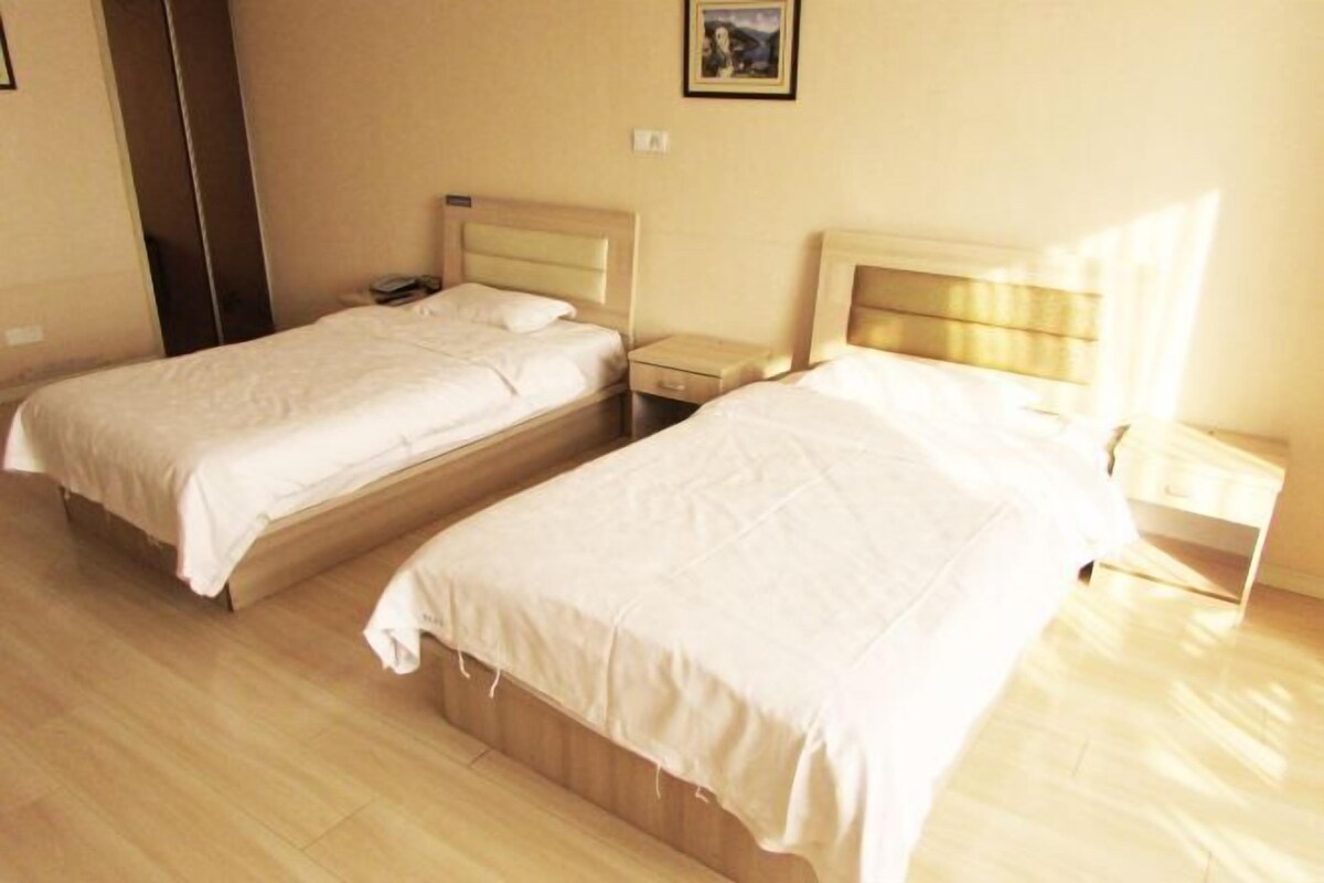 A hotel room with two single beds, wooden flooring, and a small bedside table with a lamp.