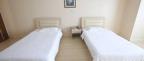 Quarto de hotel com duas camas de solteiro, uma pequena mesa de cabeceira com abajur e um quadro na parede.