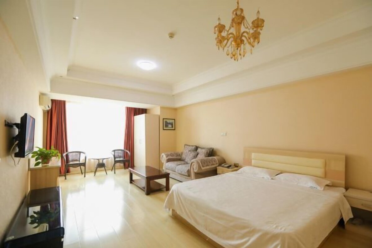 A hotel room with a large bed, a desk, a chair, a sofa, and a chandelier.