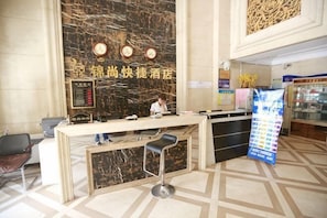A hotel reception desk with a marble wall, a digital clock, and a bar area with stools. - Jinshang Express Motel (Shenyang)
