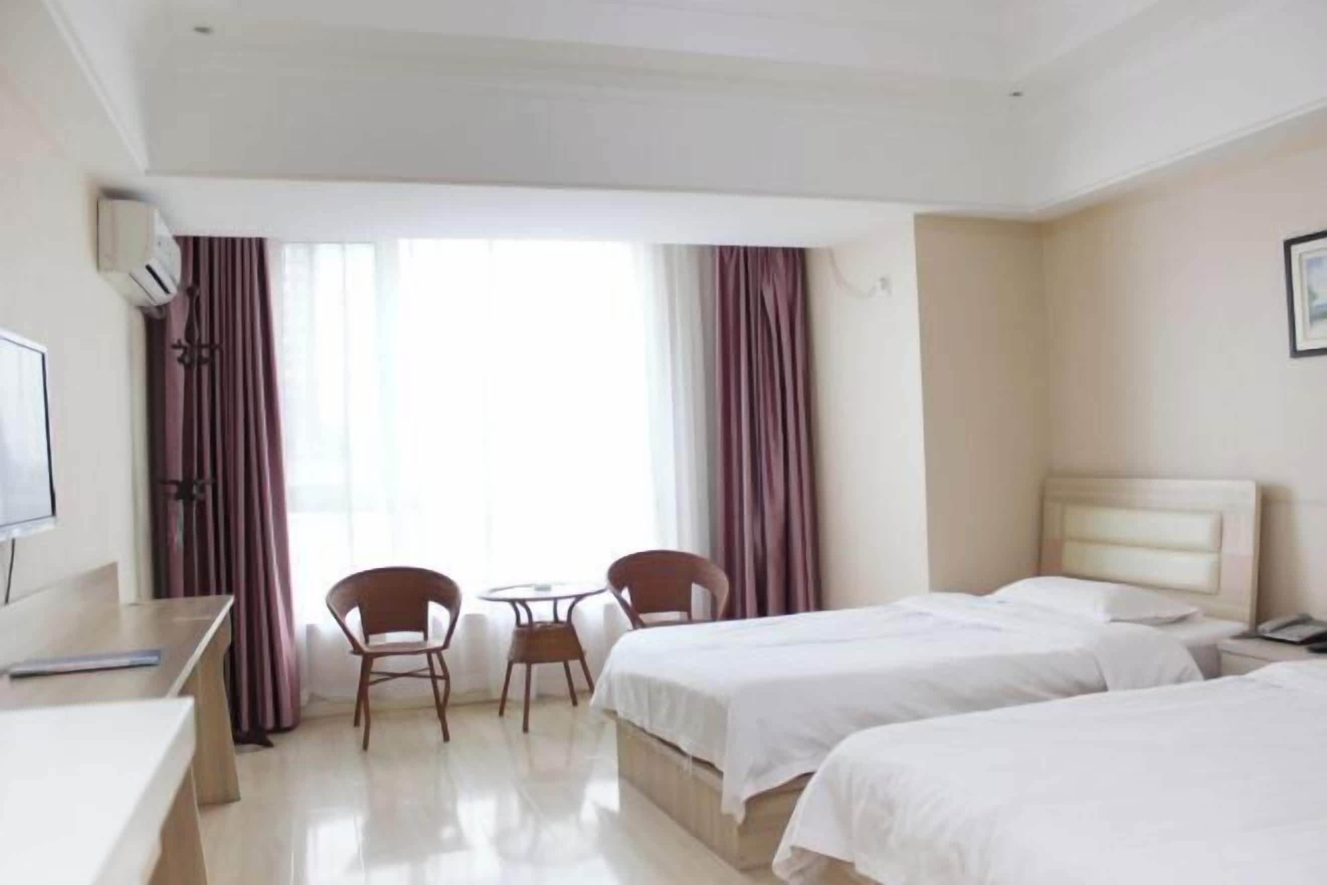 A hotel room with two beds, a desk, a chair, a small table, and a TV.
