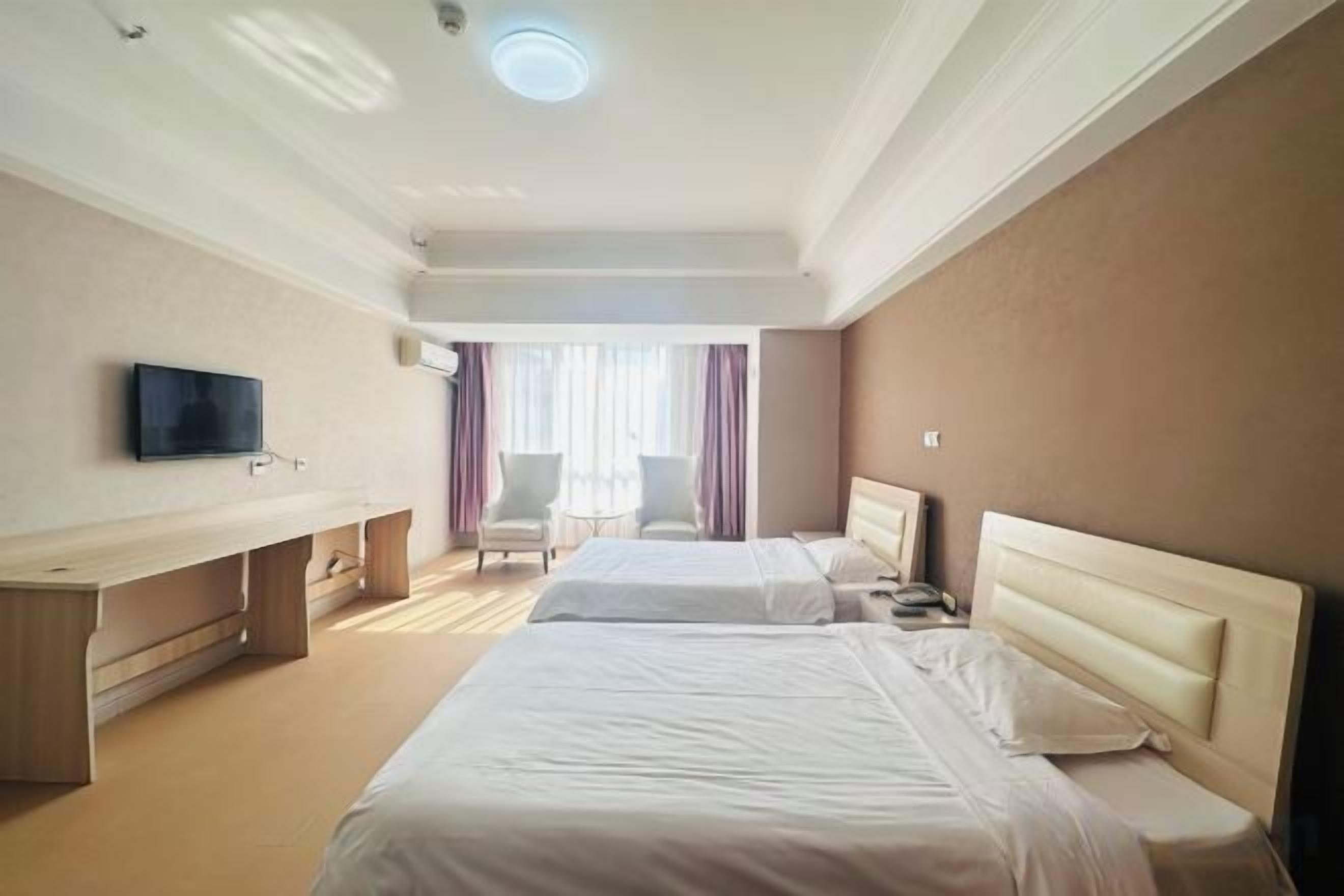 A hotel room with two beds, a desk, a chair, and a television.