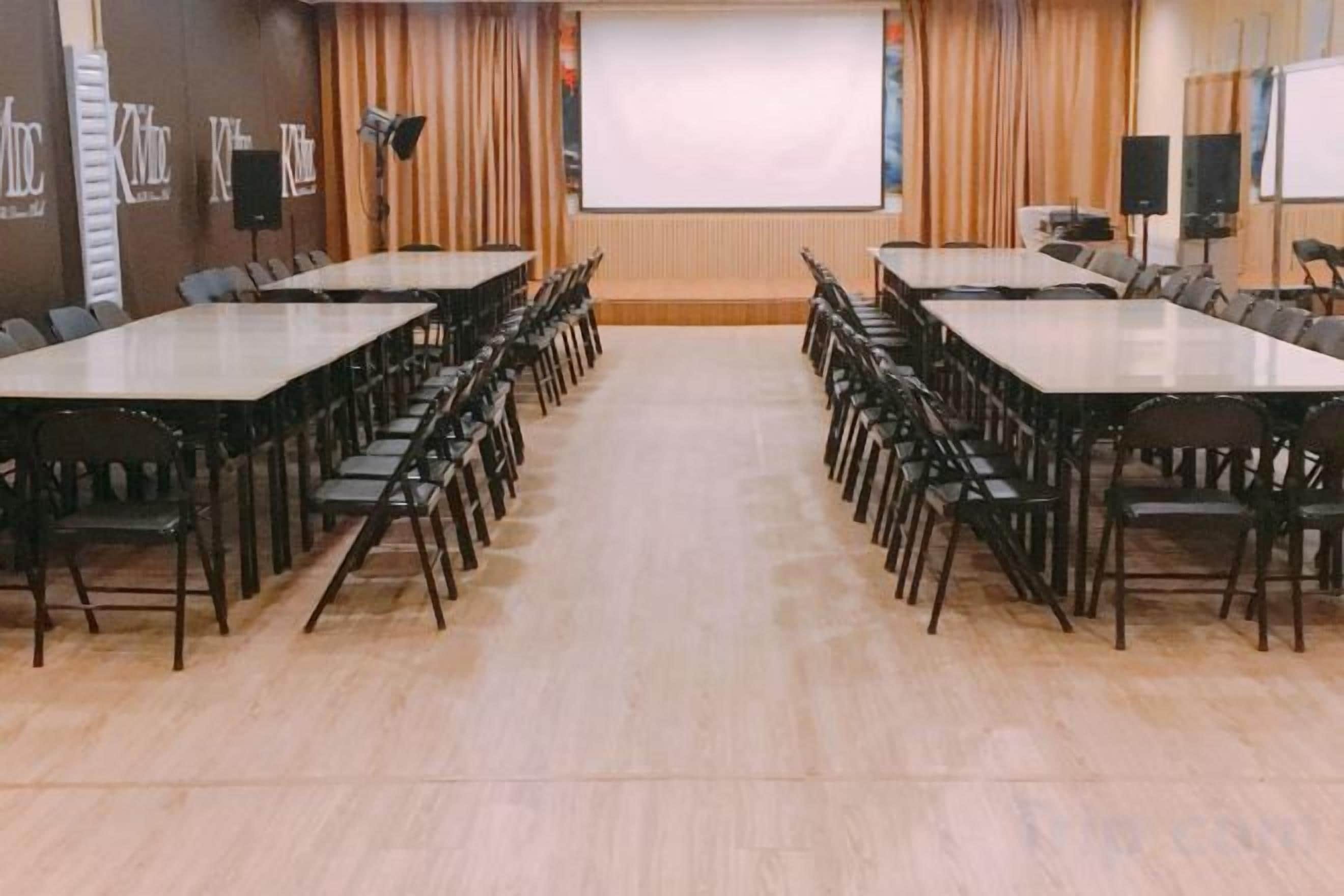 Ein Konferenzraum mit langen Tischen und Stühlen, einer Projektionsleinwand und einer Whiteboard-Tafel.