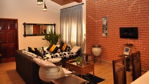 Een woonkamer met een bank, salontafel en stoelen, een televisie bevestigd aan een bakstenen muur en een plafondventilator.