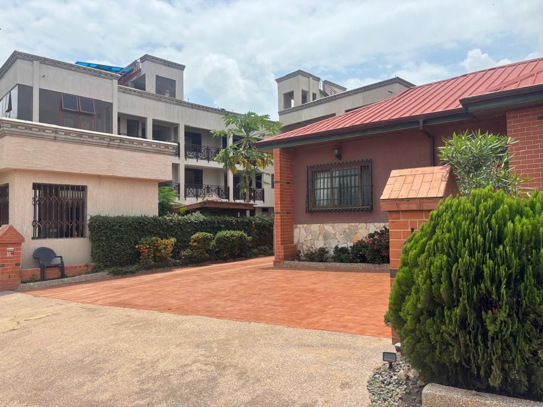 Un quartier résidentiel avec une allée pavée, une maison en briques avec un toit rouge et, au fond, un immeuble à plusieurs étages.