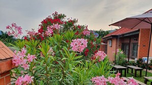Een tuin met roze bloemen, een bakstenen muur en een gebouw met een rood dak.