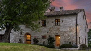 A stone building with a central arched doorway, multiple windows, and a small porch area with plants. - Checello 12 by Marche Holiday Villas (Cagli)