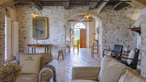 A rustic interior with stone walls, a dining area with wooden furniture, and a view through an archway. - Checello 12 by Marche Holiday Villas (Cagli)