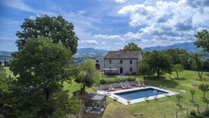 A stone house with a swimming pool, surrounded by lush greenery and mountains in the background. - Checello 12 by Marche Holiday Villas (Cagli)