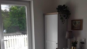 A room with a sliding glass door leading to an outdoor area, a white wardrobe, a small table with a red object, and a lamp on a white stand. - House on the lake right side 200 meters to the beach  (Klein Labenz)