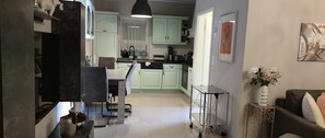 A modern kitchen with light green cabinets, a dining area with a table and chairs, and a small side table with a vase.