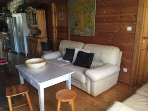 L’intérieur chaleureux d’un chalet avec une table à manger en bois, deux tabourets, un canapé avec des coussins, une carte accrochée au mur et un coin cuisine doté de placards et d’appareils électroménagers.