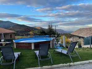 Un espace piscine avec vue sur les montagnes, une terrasse en bois et deux chaises longues.