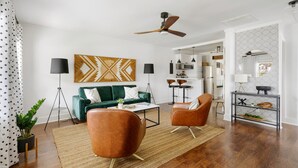 Ein modernes Wohnzimmer mit einem grünen Sofa, zwei braunen Sesseln, einem Couchtisch und einem Deckenventilator.