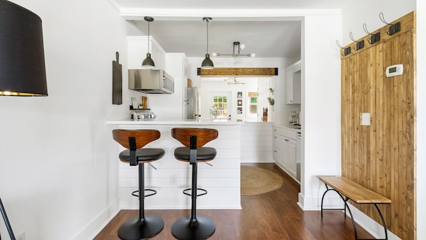 Eine moderne Küche mit weißen Schränken, einer Holzinsel mit zwei Barhocker, Pendelleuchten und einer Akzentwand aus Holz.