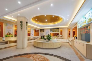 A hotel lobby with a central reception desk, a circular seating area, and a counter with a menu display.