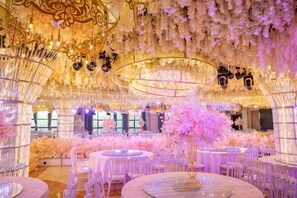 A banquet hall with round tables, floral arrangements, and chandeliers.