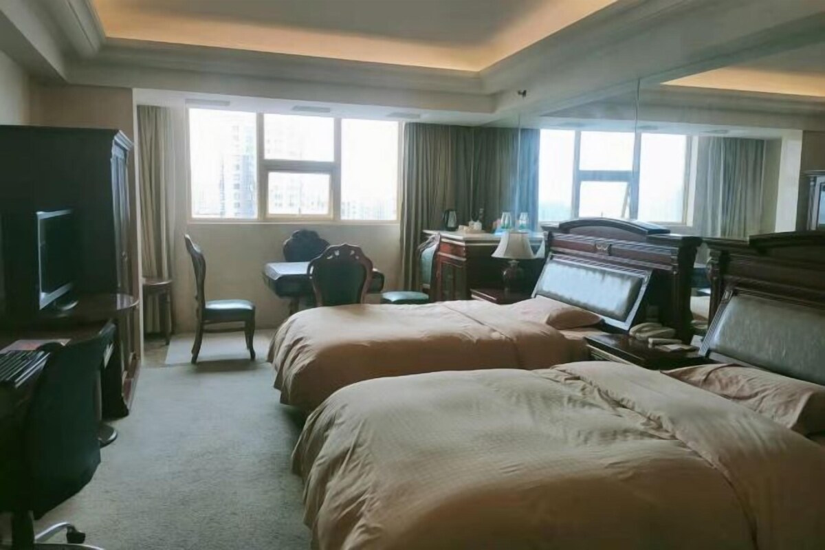A hotel room with two beds, a desk, a chair, a television, and a window with curtains.