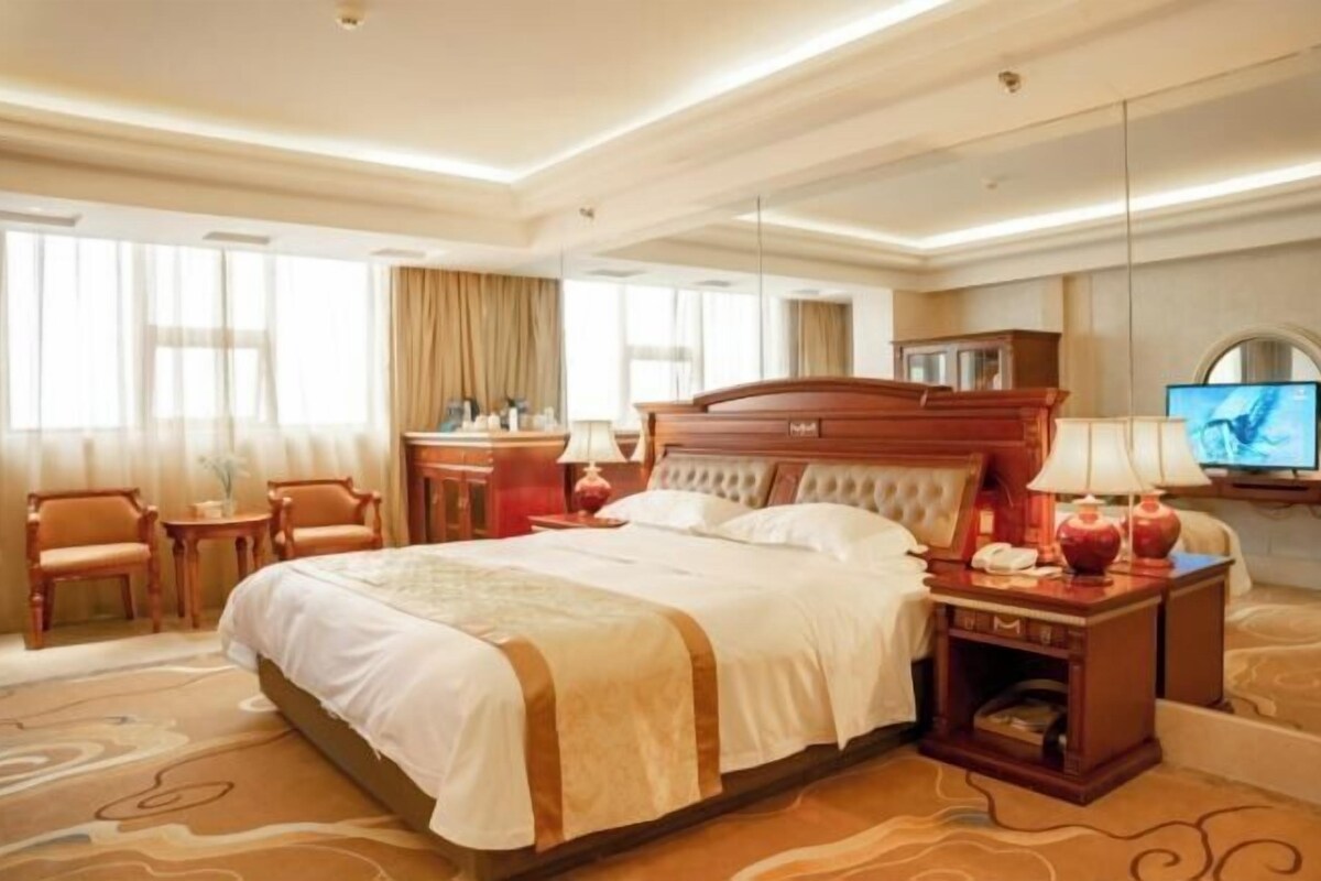 A hotel room with a large bed, a desk, a chair, a TV, and a mirror.