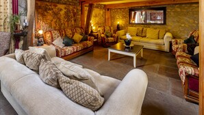 A cozy living room with a stone wall, wooden beams, and a variety of seating options including a sofa, armchairs, and a loveseat. - Authentic 100 year old barn, indoor pool (Gouttières)