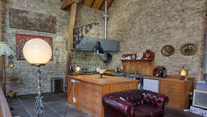 A rustic kitchen with stone walls, wooden cabinets, a central island, and a leather sofa. - Authentic 100 year old barn, indoor pool (Gouttières)
