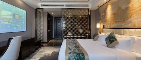 A modern hotel room with a large bed, a desk, and a screen displaying room options.