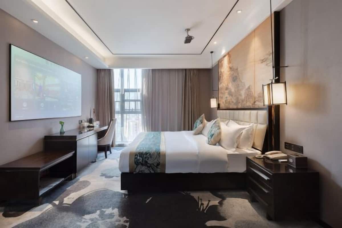 Une chambre d’hôtel moderne dotée d’un grand lit, d’un bureau, d’une télévision et d’une grande fenêtre.