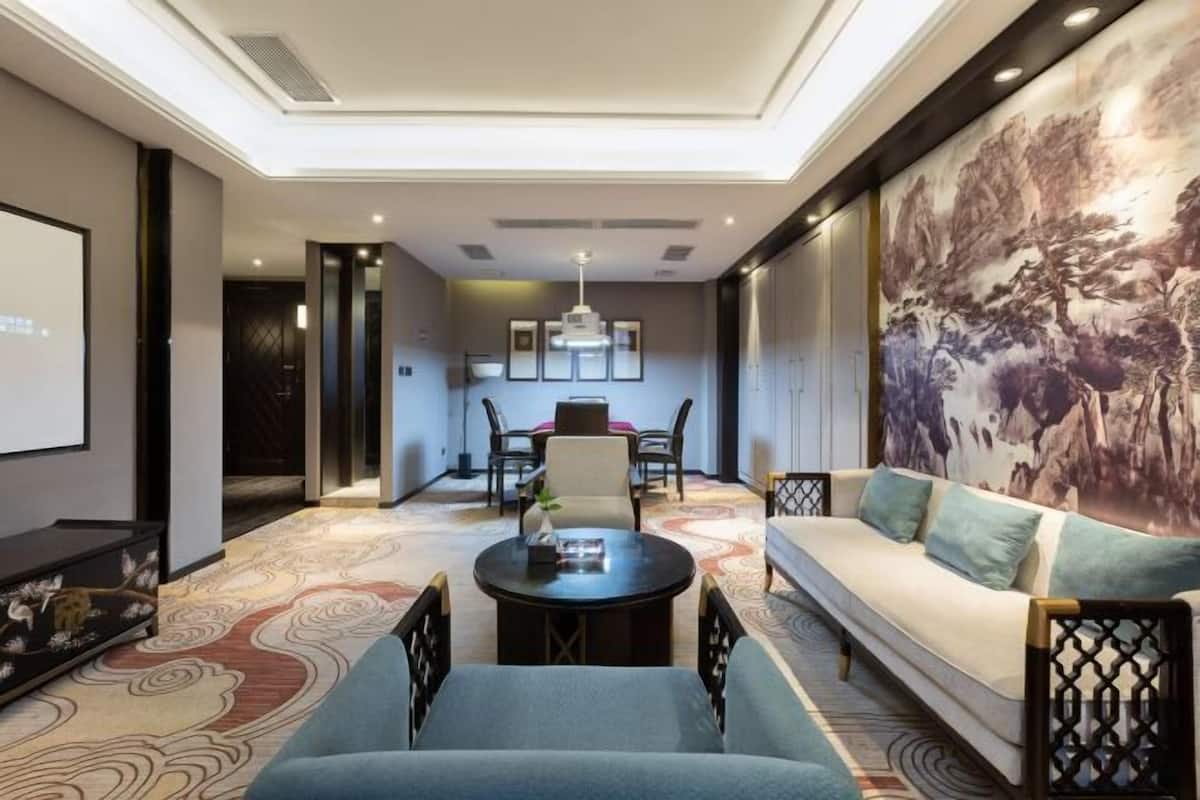 Une chambre d’hôtel moderne, dotée d’un canapé, d’une table basse, d’un coin repas avec des chaises et d’un grand tableau au mur.